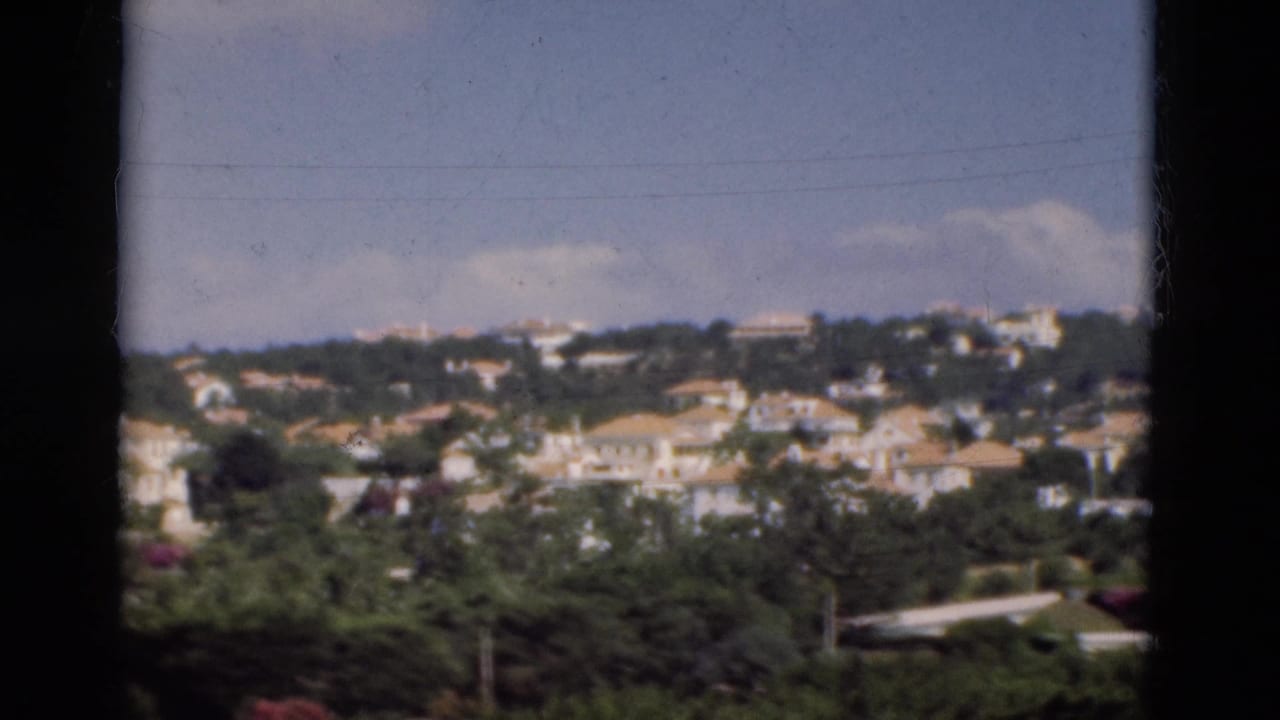 Elevated view of hillside houses and trees under a blue sky.