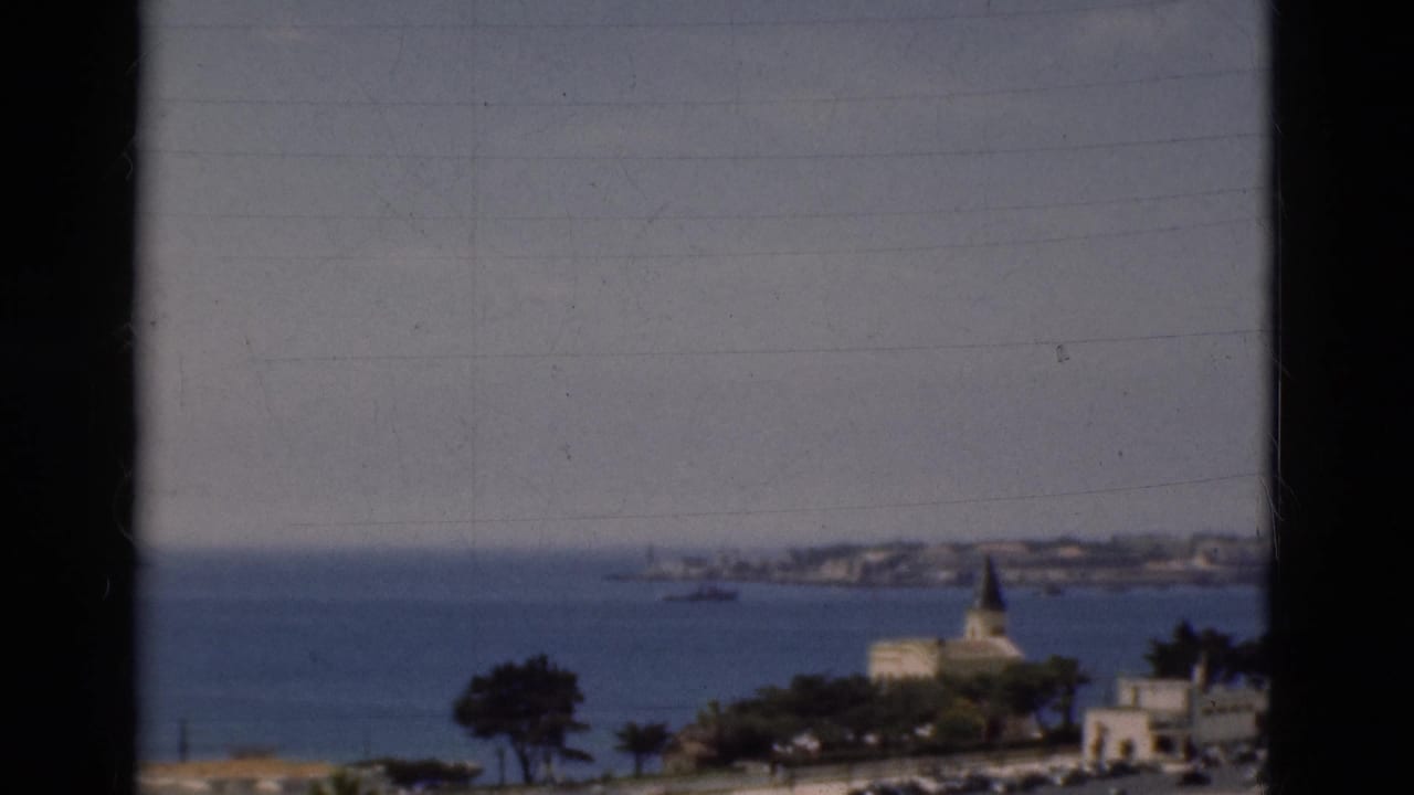 Blue bay with a church spire, distant shoreline, hazy sky, and dark frame edges.