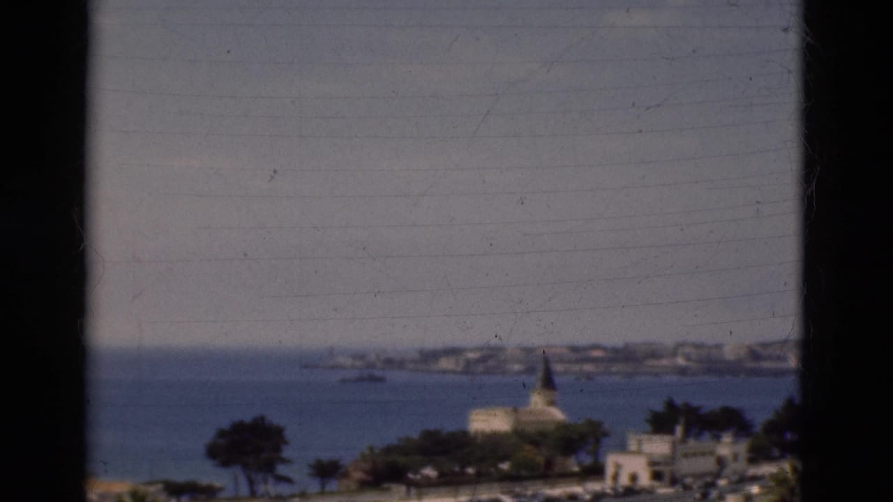 1975 Portugal home-movie frame showing the bay, church spire, distant town shoreline, trees, and dark vertical framing.