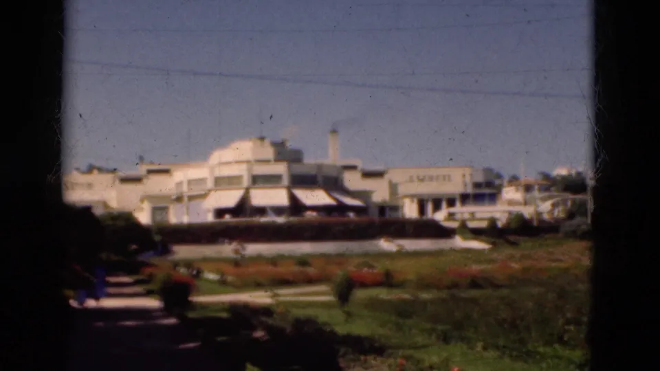 1975 Portugal 8mm view of a pale garden-fronted building with lawns, paths, flower beds, and small distant people.