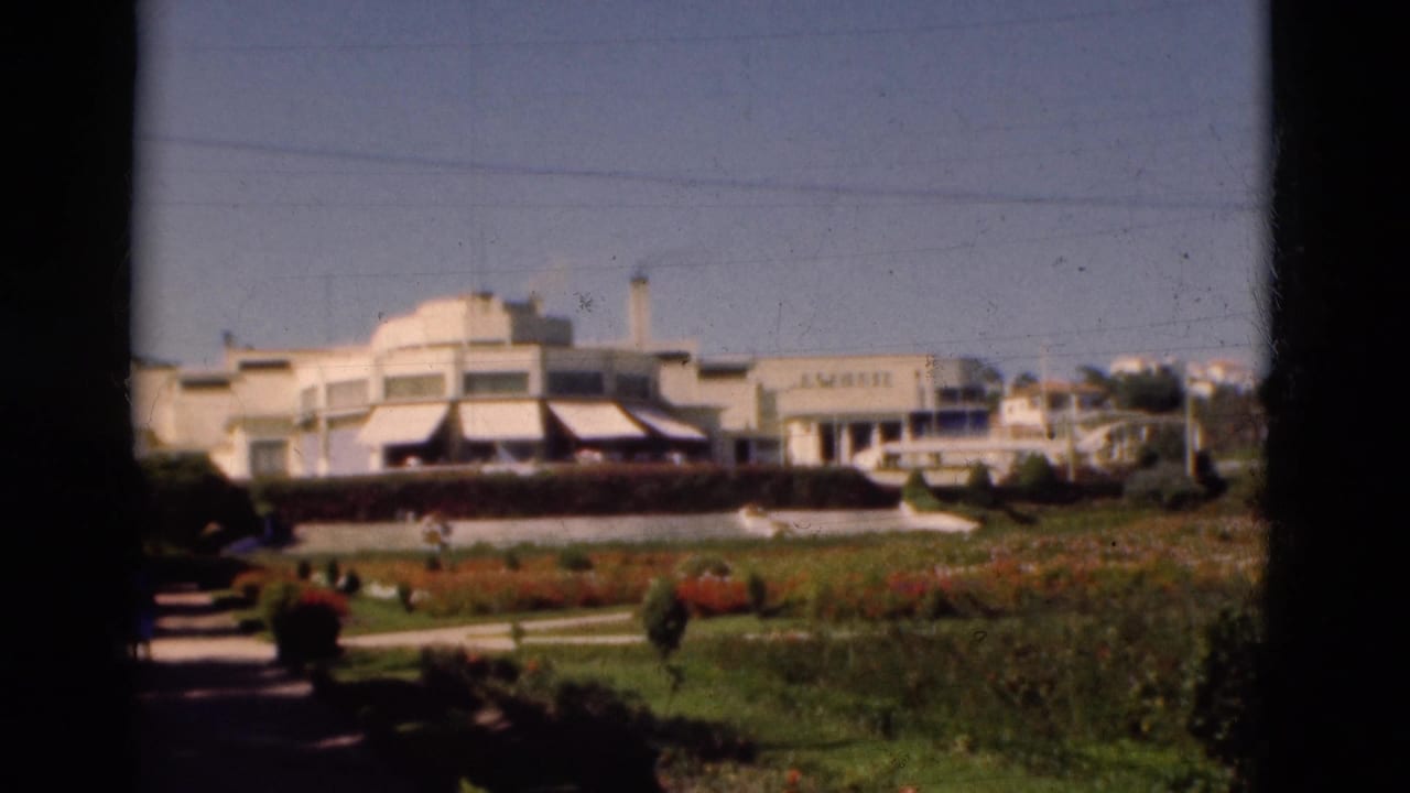 White building with striped awnings behind a landscaped garden and dark frame borders.