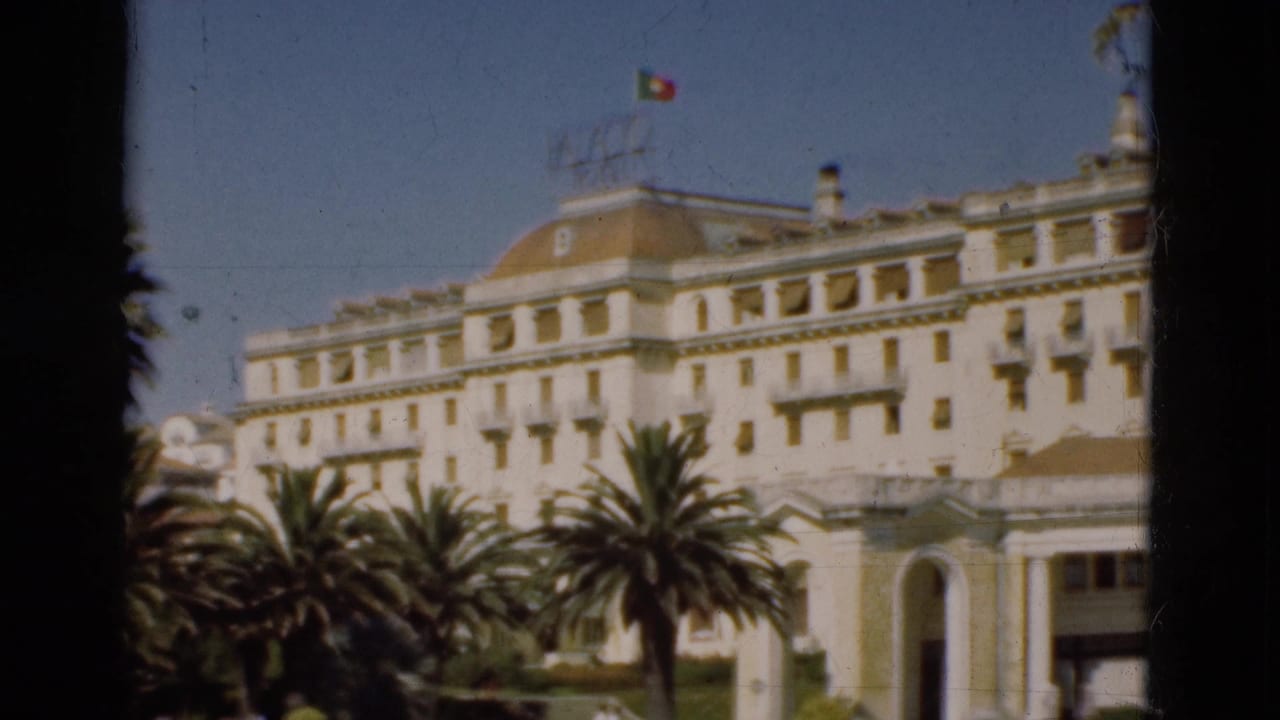 White multi-story building with palm trees and a Portuguese flag above the roof.