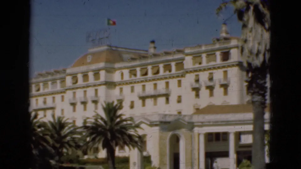 1975 Portugal 8mm frame showing the white civic-looking facade with balconies, palm trees, and an arched entry structure.