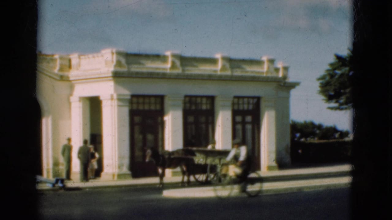 1975 Portugal 8mm frame showing a white classical-looking building, several pedestrians, and a horse-drawn cart passing in front.