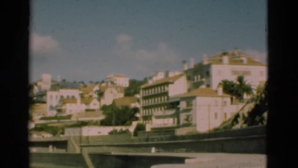 1975 Portugal 8mm frame showing a soft, panning view of hillside buildings, trees, and a low wall along the foreground.