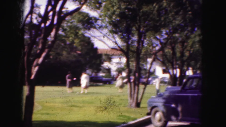 A Florida lawn scene from 1975 shows distant people near trees and a parked dark car, viewed through the same home-movie framing.