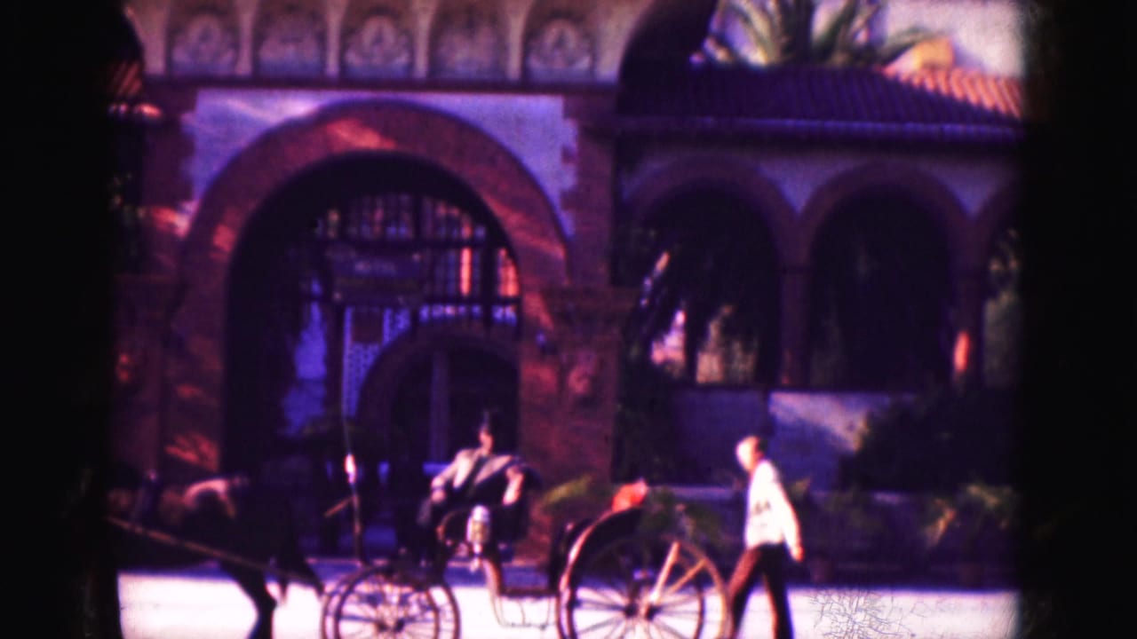 Horse-drawn carriage waits near an arched building as a man walks past.