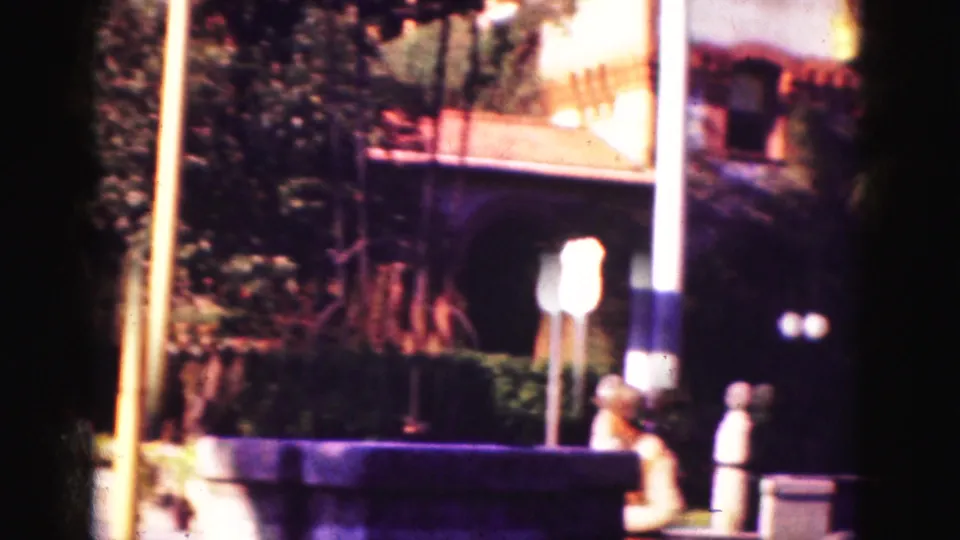 1975 Florida home-movie frame showing a sunlit roadside area with signs, palms, shrubs, and people near an attraction entrance.