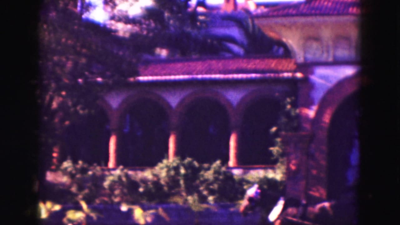Arched colonnade and tiled roof partly screened by trees and shrubs.