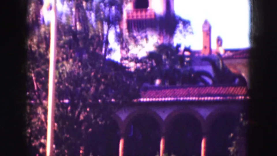 1975 Florida home-movie view of a bell tower and arched architecture seen through trees, with strong sunlight and soft 8mm focus.