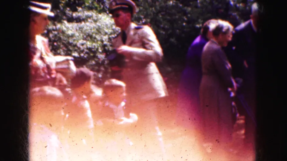 Brief 1975 Florida home-movie view of adults gathered outdoors in bright sun, with trees and strong film flare visible.