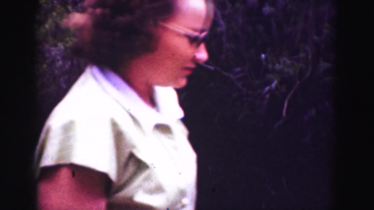 Woman in glasses and a light collared shirt walking beside trees.
