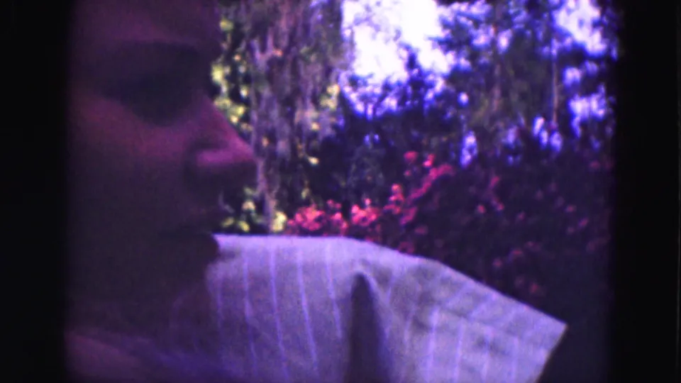 Young woman in profile during a 1975 Florida Everglades home movie, with pink flowers and greenery behind her.