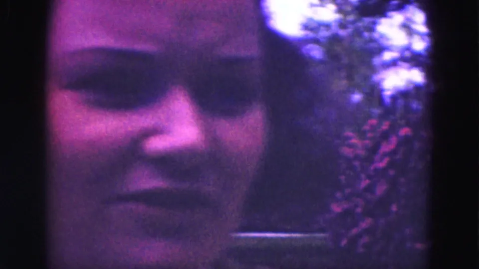 Close home-movie view of a young woman's face in 1975 Florida Everglades vacation footage, with foliage in the background.
