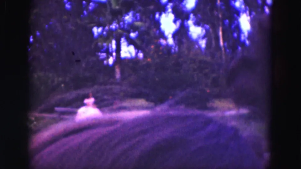 Soft 8mm view of a woman in white seated near a bench across canal water during a 1975 Florida Everglades trip.