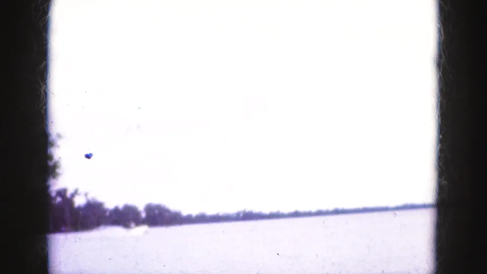 Wide Florida Everglades water view from the 1975 home movie, with a bright sky and low distant tree line.