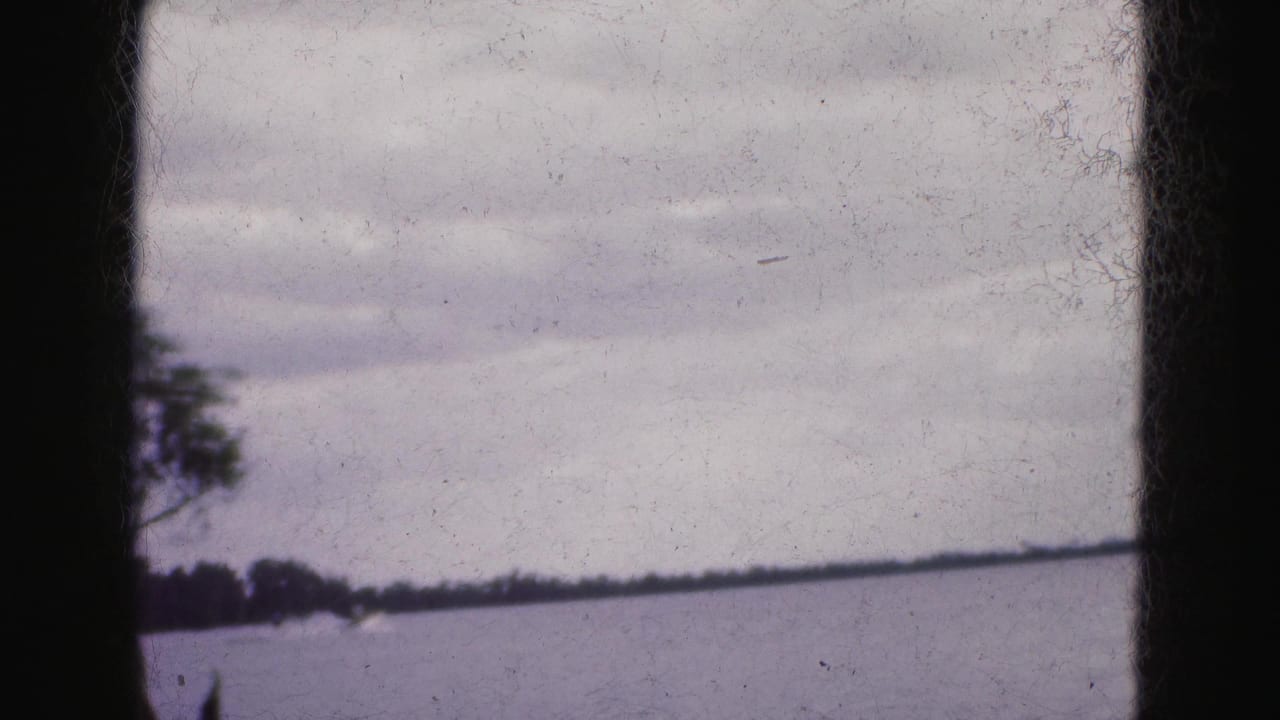 1975 Florida Everglades home-movie frame showing a wide lake surface, low shoreline, trees, and dark film gate edges.