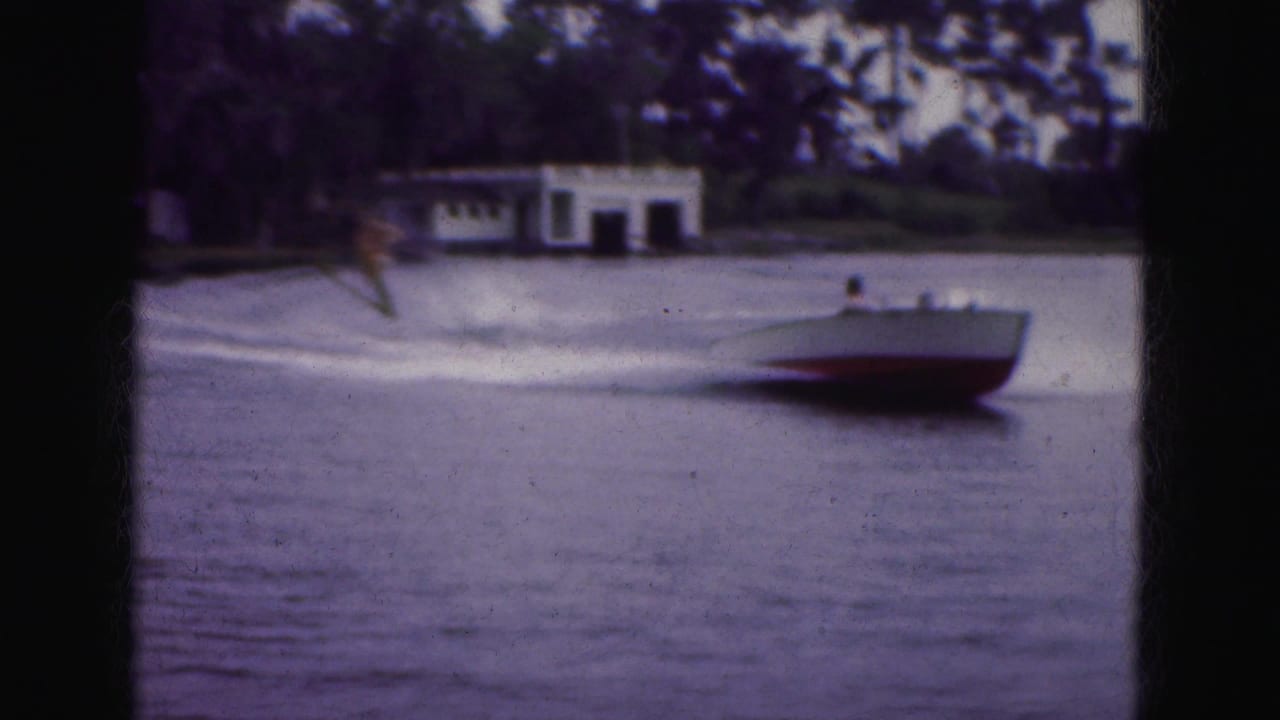 Motorboat moves across a Florida Everglades lake in 1975, with a small white building and trees along the shore.