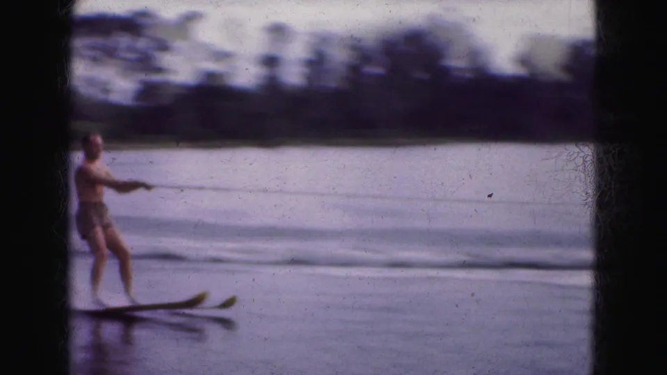 1975 Florida Everglades home-movie frame of a man water skiing across a calm lake, filmed with soft focus and faded color.