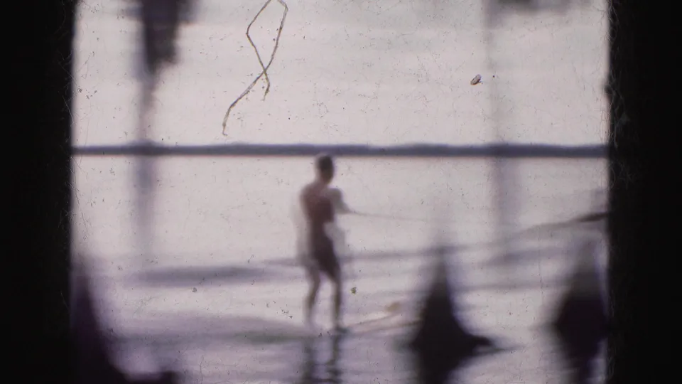 Soft 1975 Florida Everglades frame showing a distant water skier on a pale lake with film scratches and dark gate edges visible.