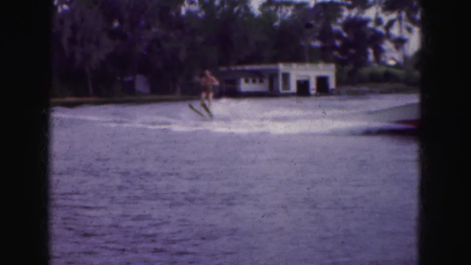 The skier appears unsteady behind the boat as wake spreads across the lake in 1970s Florida Everglades footage.