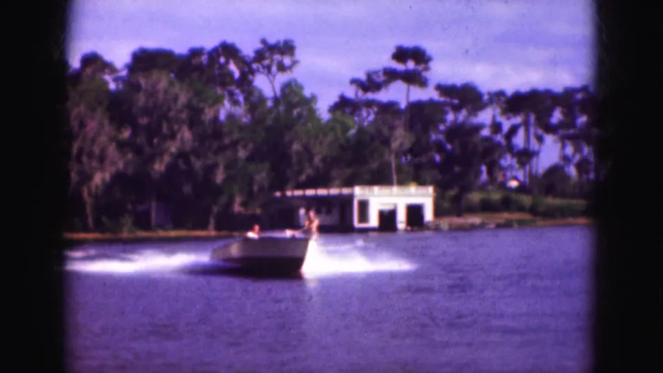The boat passes in the foreground while the skier appears to drop into the wake in this 1975 Florida waterskiing scene.