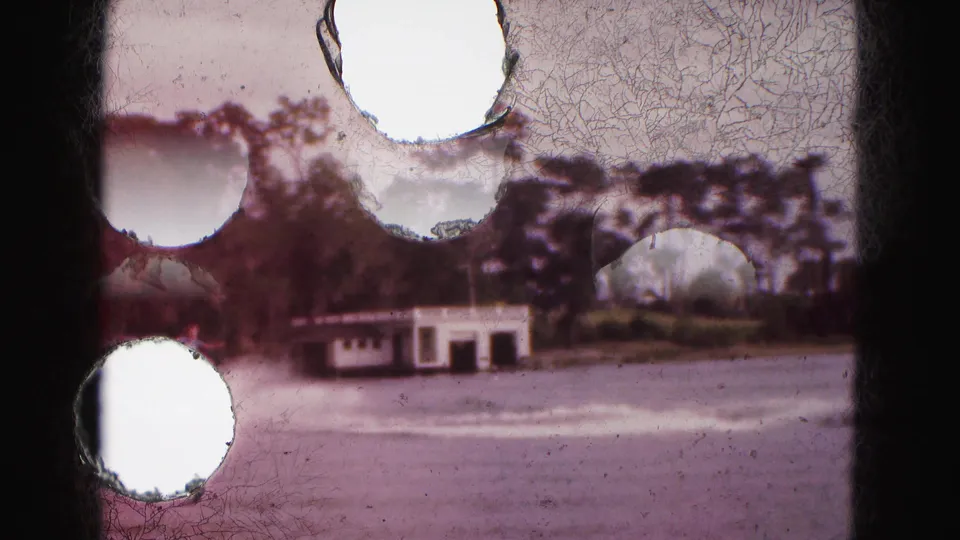 1975 Florida Everglades 8mm frame with a motorboat passing a white boathouse, partly obscured by film damage and frame borders.