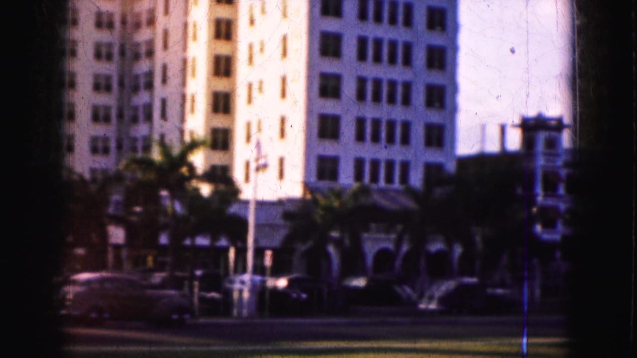 Soft 8mm view of Florida street traffic, palm trees, and sunlit multi-story buildings from the 1975 reel.