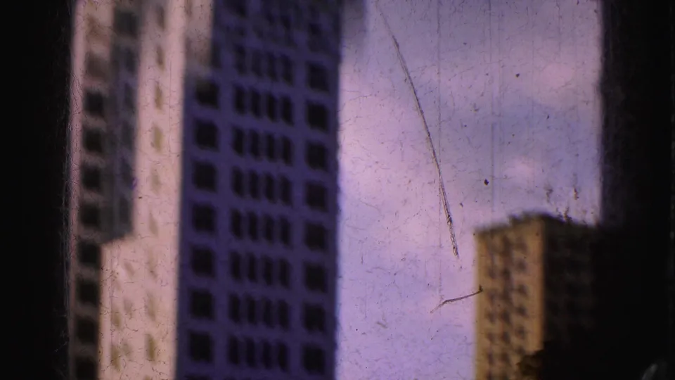 Soft, scratched 8mm frame from the 1975 Florida footage showing tall buildings and a smaller sunlit structure.