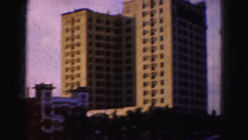 1975 Florida travel footage appears to show tall waterfront buildings under a pale sky, with soft focus and 8mm gate edges.