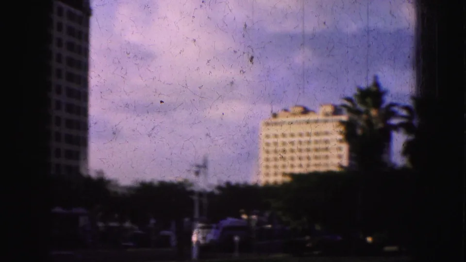 A high-rise building and palm tree appear beyond a dark shoreline area in this soft 1970s Florida home-movie frame.