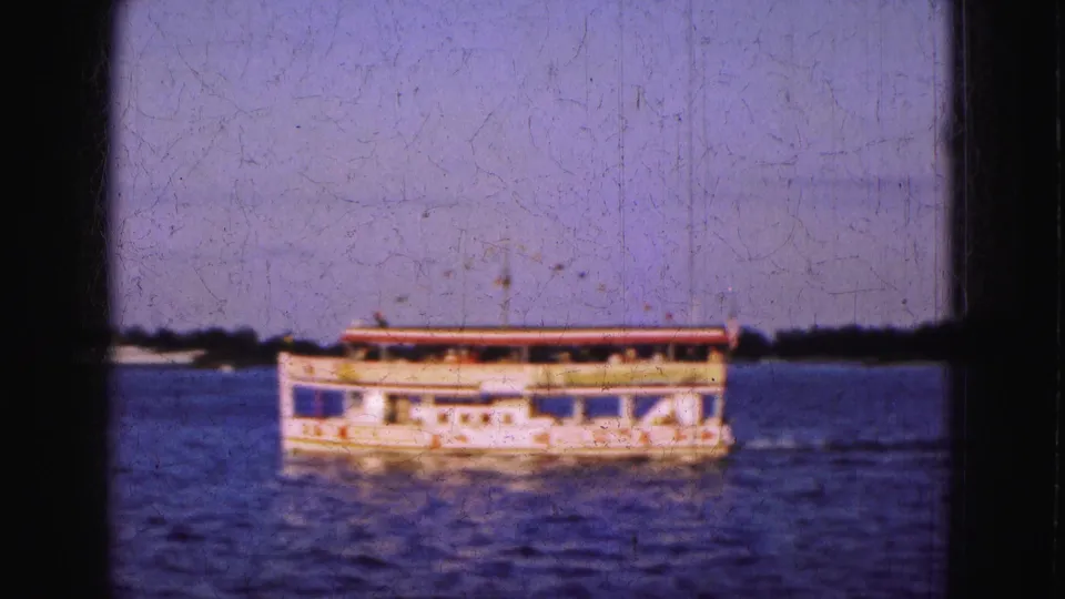 A low river or excursion boat crosses open water in 1975 Florida 8mm travel footage, with horizon and soft film wear visible.