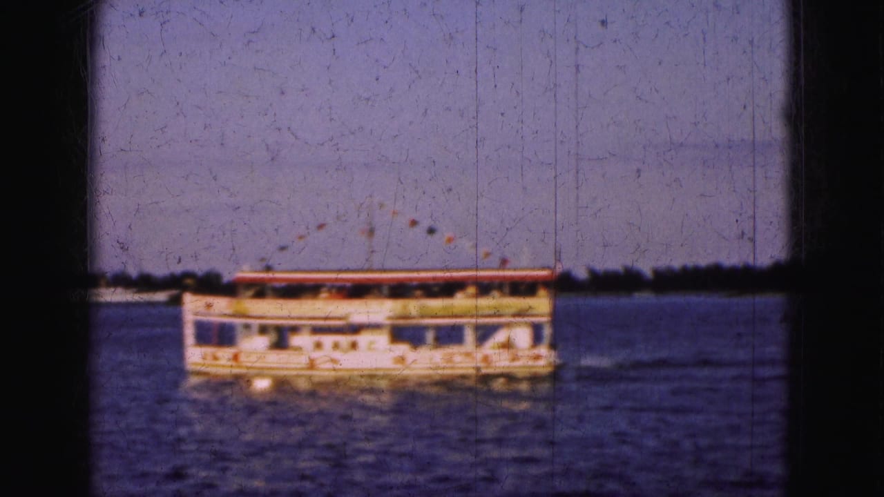 Paddlewheel-style boat crossing calm water behind dark window framing.