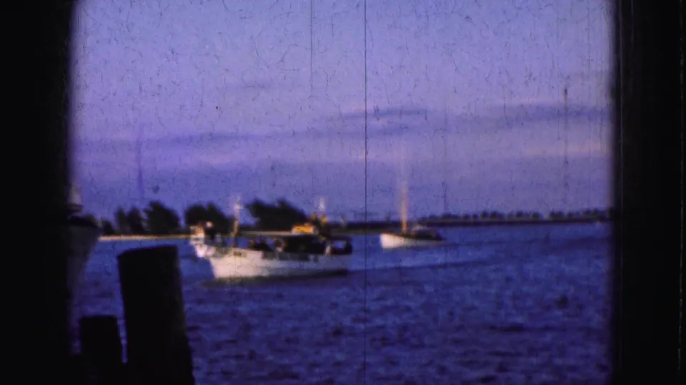 1975 Florida Everglades frame showing small boats, sailboats, and dock posts across a calm blue waterway.