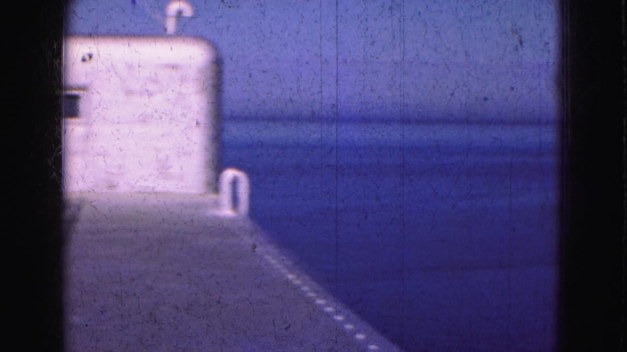 White dockside structure at the edge of calm blue water with dark film borders.