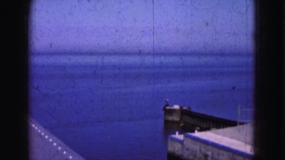 1975 Florida Everglades frame with open blue water, a low horizon, and part of a dock or railing at the right edge.