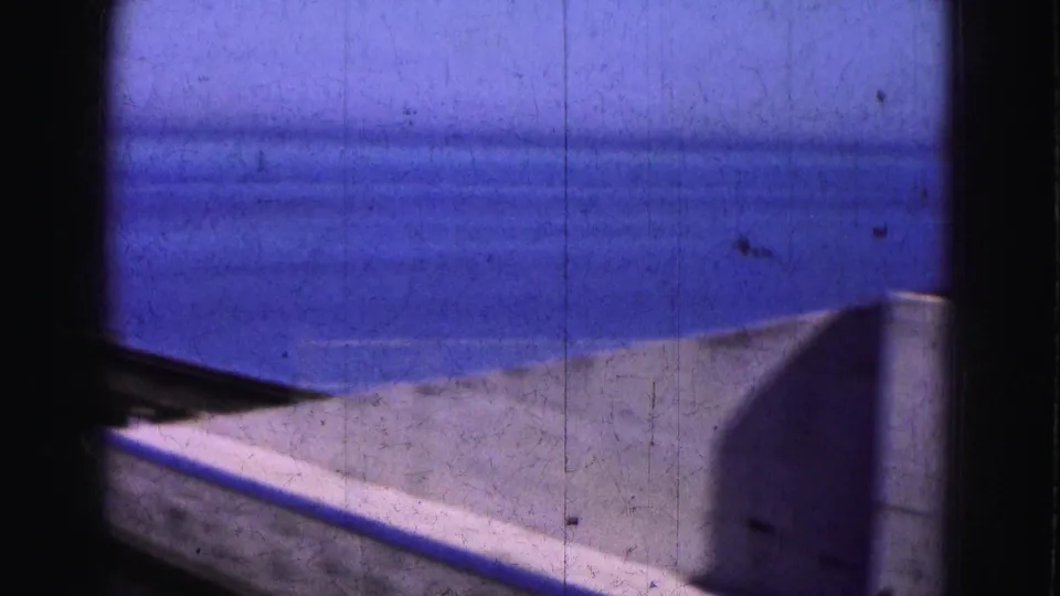 1975 Florida Everglades home-movie frame showing a dock surface and low wall against calm blue water.