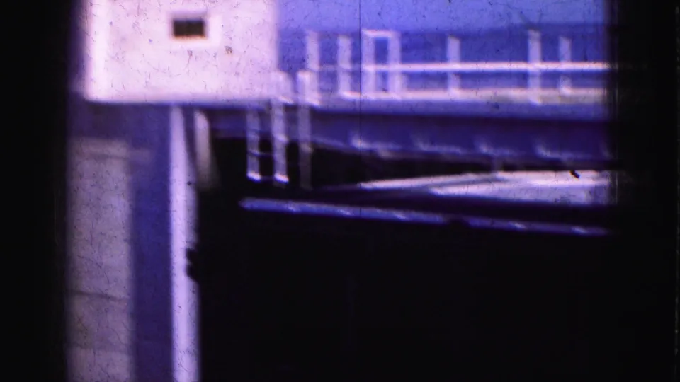 1975 Florida Everglades frame showing a white dockside building with railings and a dark shadowed area below.