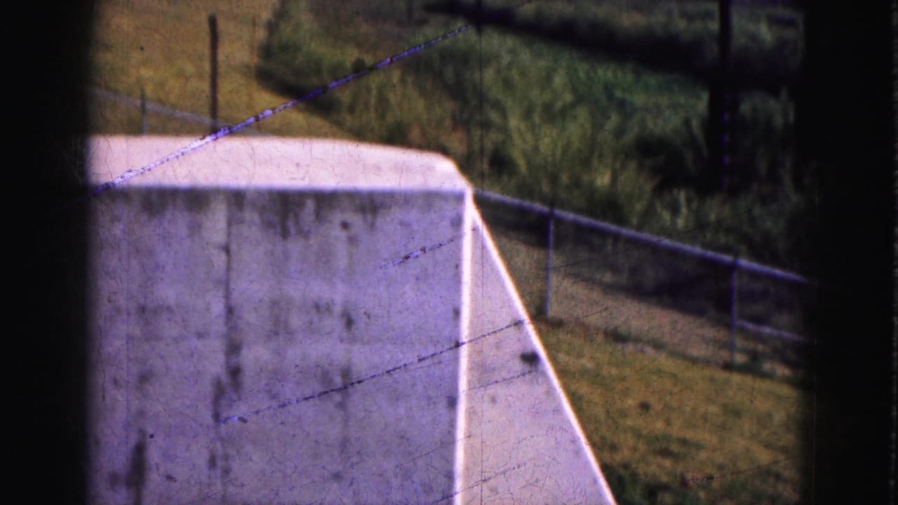 White concrete wall, fence posts, and utility line seen from a moving viewpoint in the 1975 Florida Everglades travel footage.