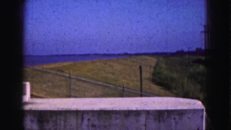 Open Florida Everglades field under blue sky, with a white wall foreground and distant poles captured on 8mm film in 1975.