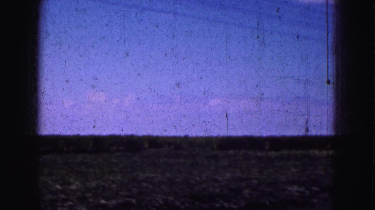 Dark window frame divides a grainy sky view over low open ground.