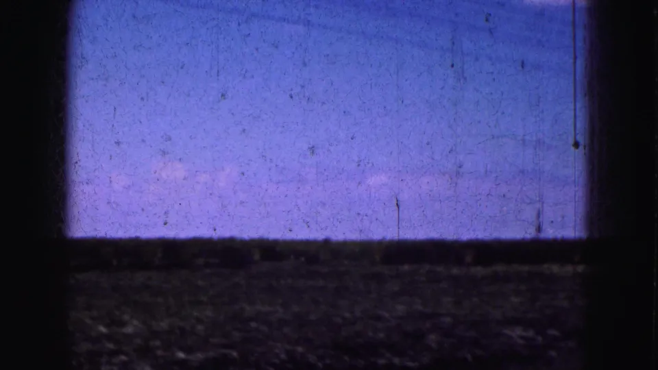 Grainy 8mm view from a moving vehicle across open Everglades ground beneath a blue-purple sky.