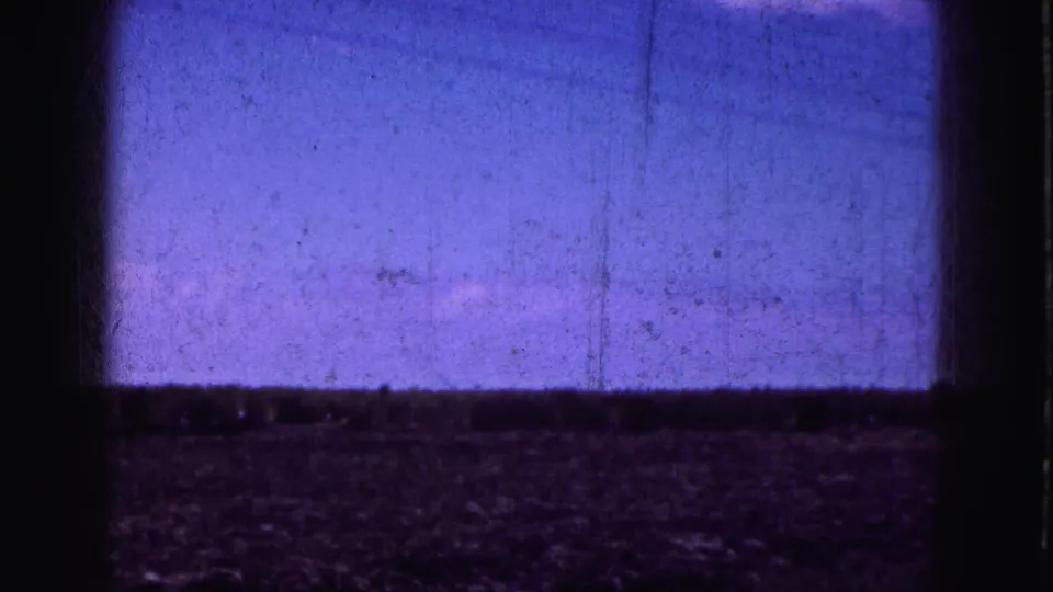 Soft 8mm frame of flat Everglades-area land and sky, partially blocked by dark vehicle-window framing.