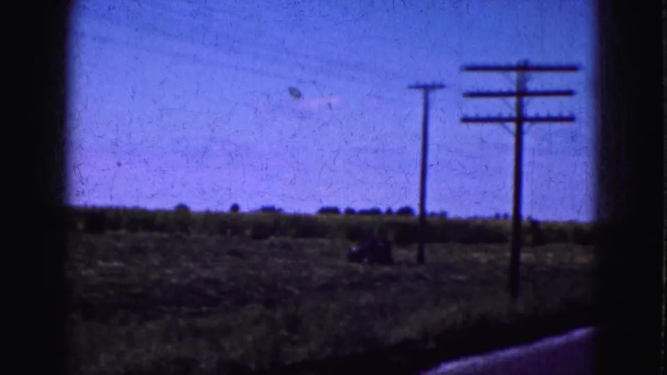 1975 8mm Florida Everglades travel view showing utility poles along an open rural roadside beneath a blue-shifted sky.
