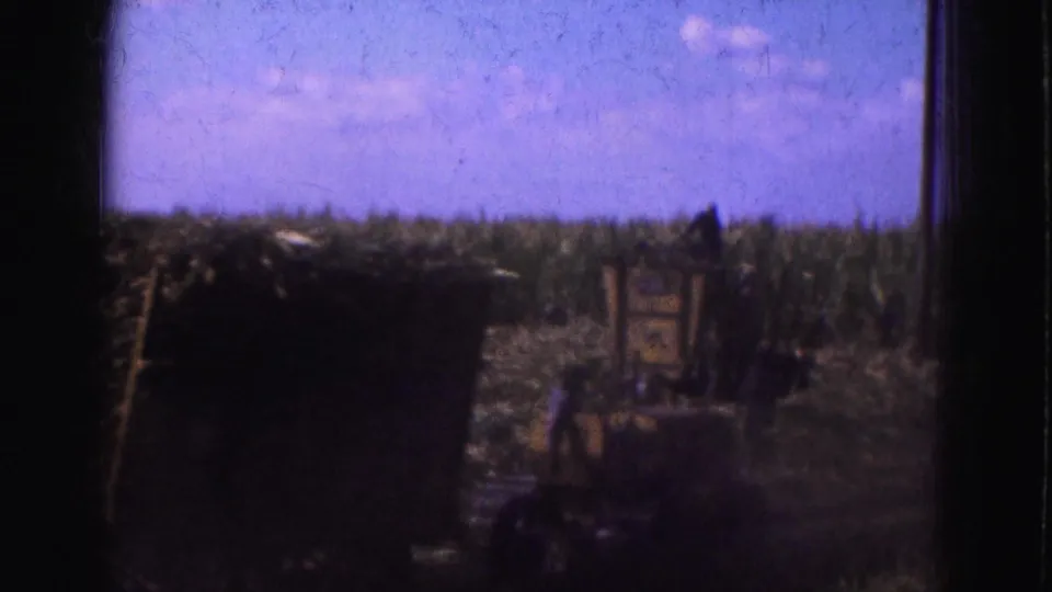 A 1975 Everglades farm view with a dark foreground stack, tall vegetation, and indistinct workers or equipment shapes.