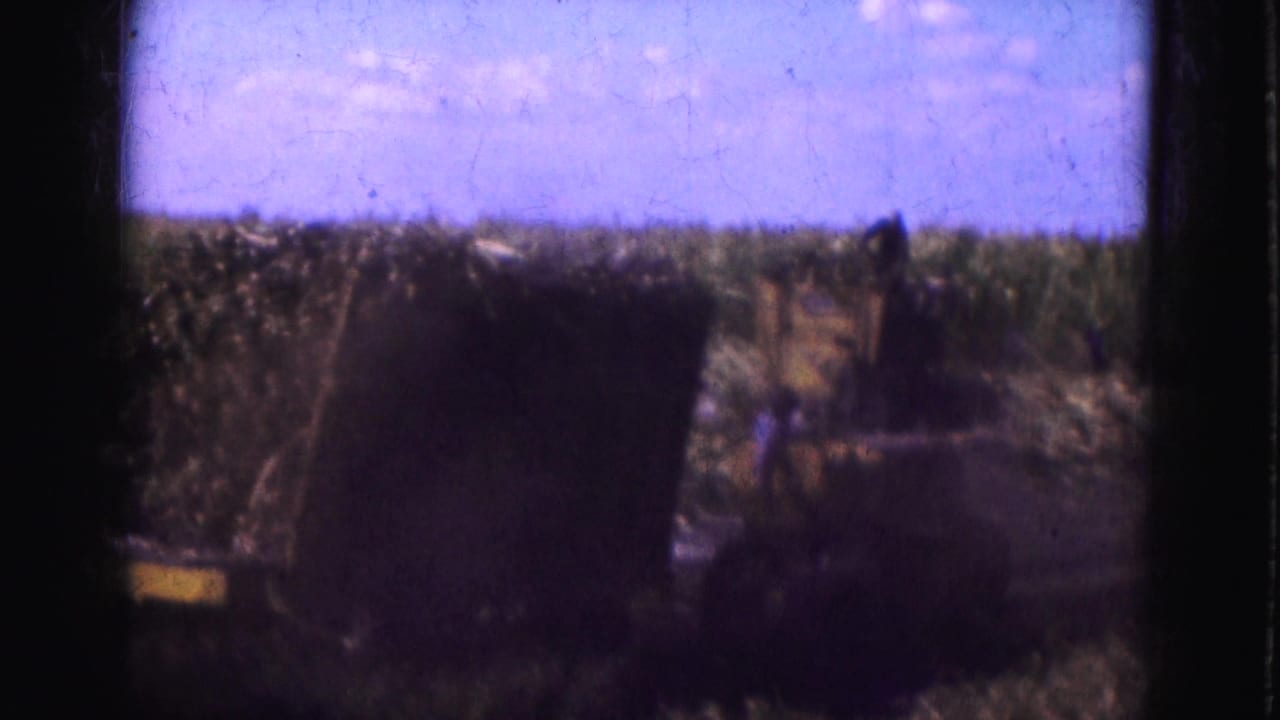 Dark farm vehicle or hay load in a field beneath a bright sky.