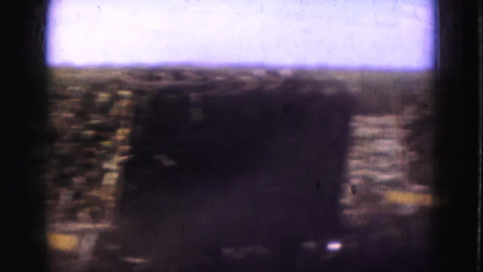 Soft 8mm frame from a Florida farm scene showing a dark hay load or vehicle near textured crop rows.