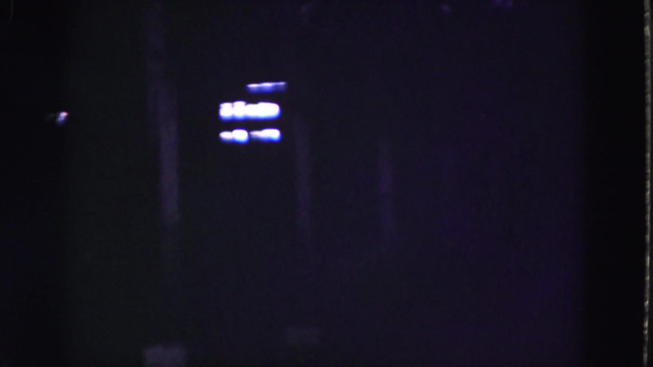 1975 8mm Florida Everglades footage showing a very dark structure with faint blue-white lights and shadowed vertical forms.