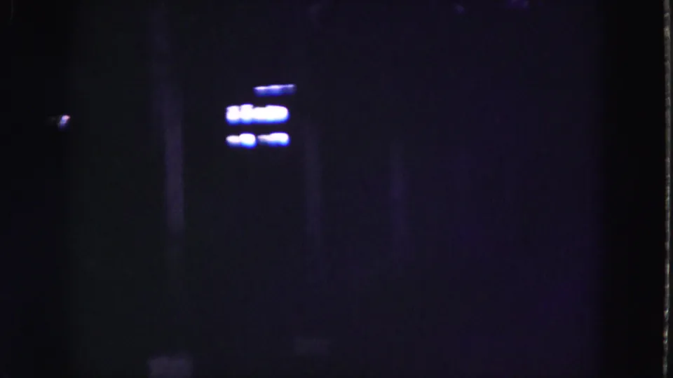 1975 8mm Florida Everglades footage showing a very dark structure with faint blue-white lights and shadowed vertical forms.