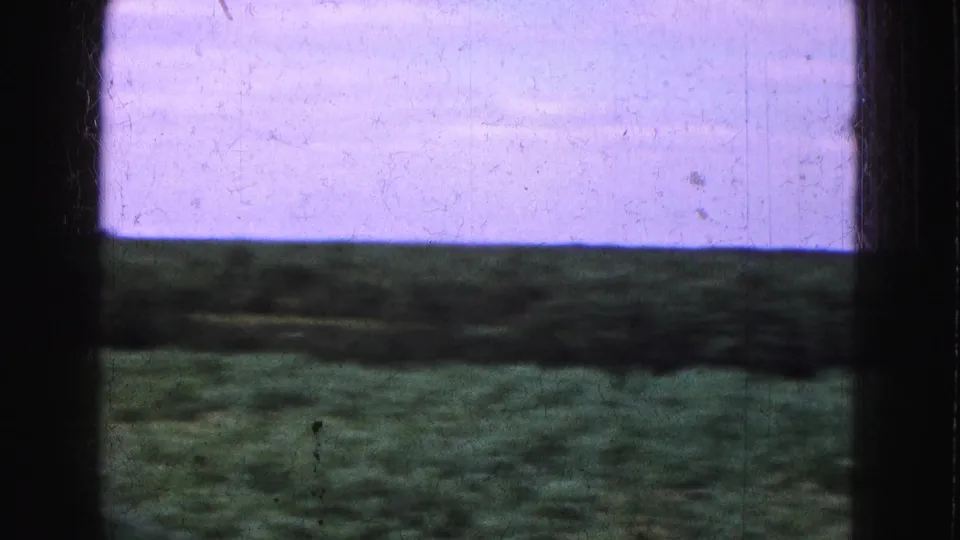 1975 Florida Everglades frame with a dark window edge, open grass, distant vegetation, and a pale purple sky.